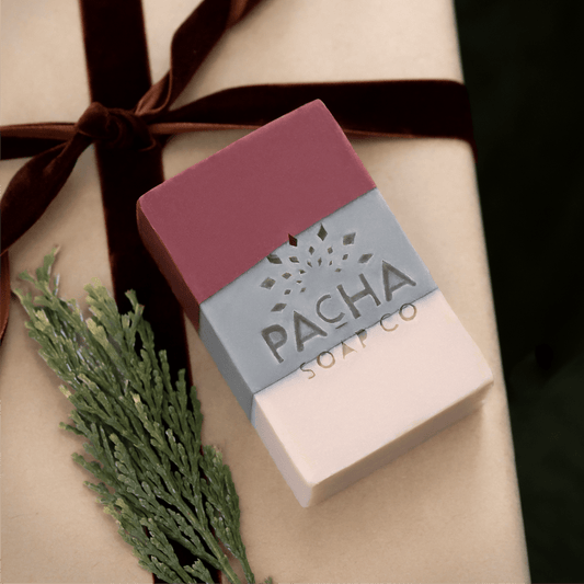 A rectangular bar of soap from Pacha Soap Co. presented on a beige gift box tied with a dark brown ribbon and decorated with a green sprig.