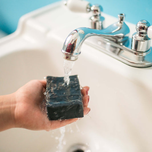 Person running Tea Tree Charcoal Facial Bar under water in sink
