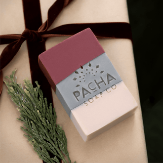 A rectangular bar of soap from Pacha Soap Co.  presented on a beige gift box tied with a dark brown ribbon and decorated with a green sprig.