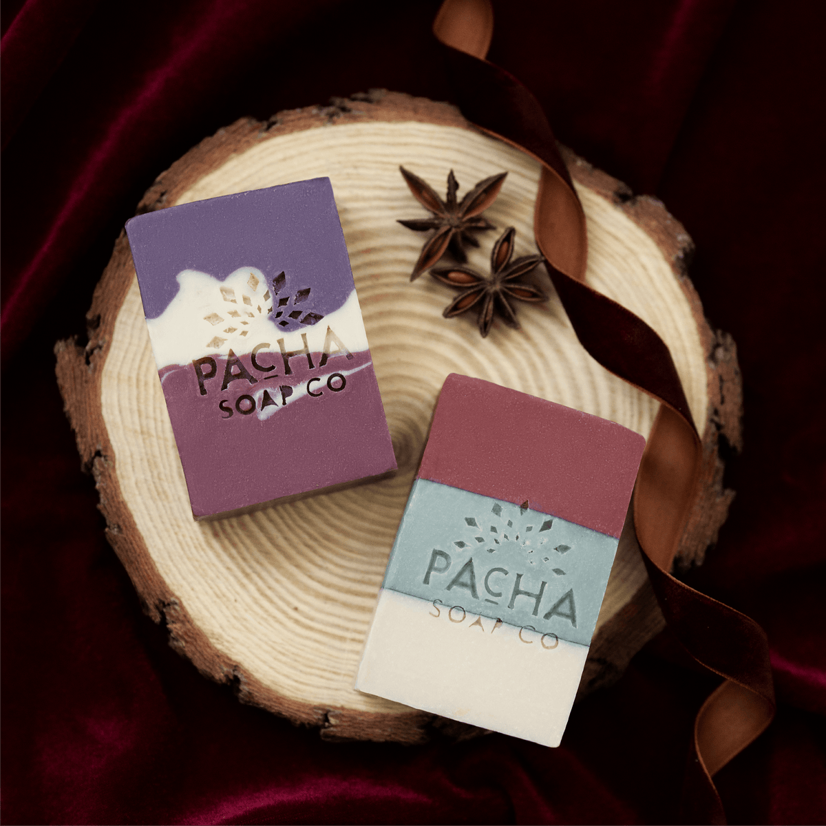 Two rectangular bars of soap from Pacha Soap Co. displayed on a rustic wood slice.