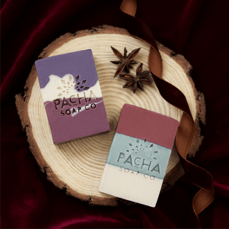 Two rectangular bars of soap from Pacha Soap Co. displayed on a rustic wood slice.