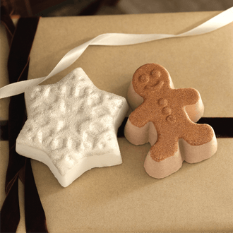 Two decorative bath bombs shaped like a white star and a gingerbread man, displayed on a brown kraft paper surface with a white ribbon.