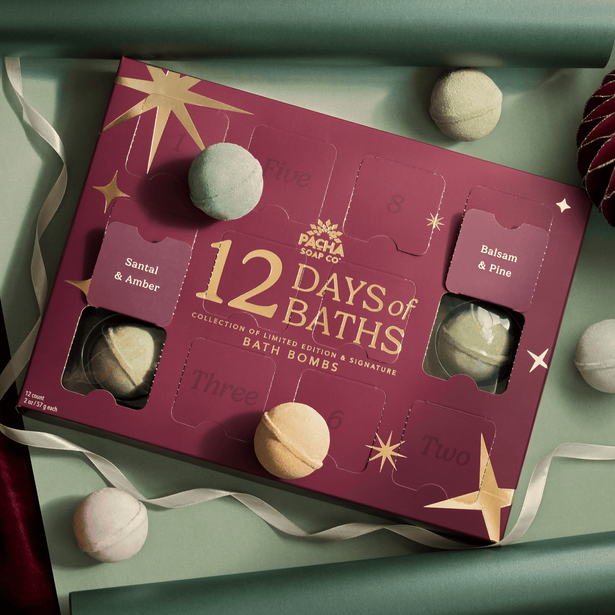 12 Days of Baths Advent Calendar with Handcrafted bathbombs made by Pacha Soap Co in a beautiful setting with bath bombs scattered around it, all along with ornaments and ribbon
