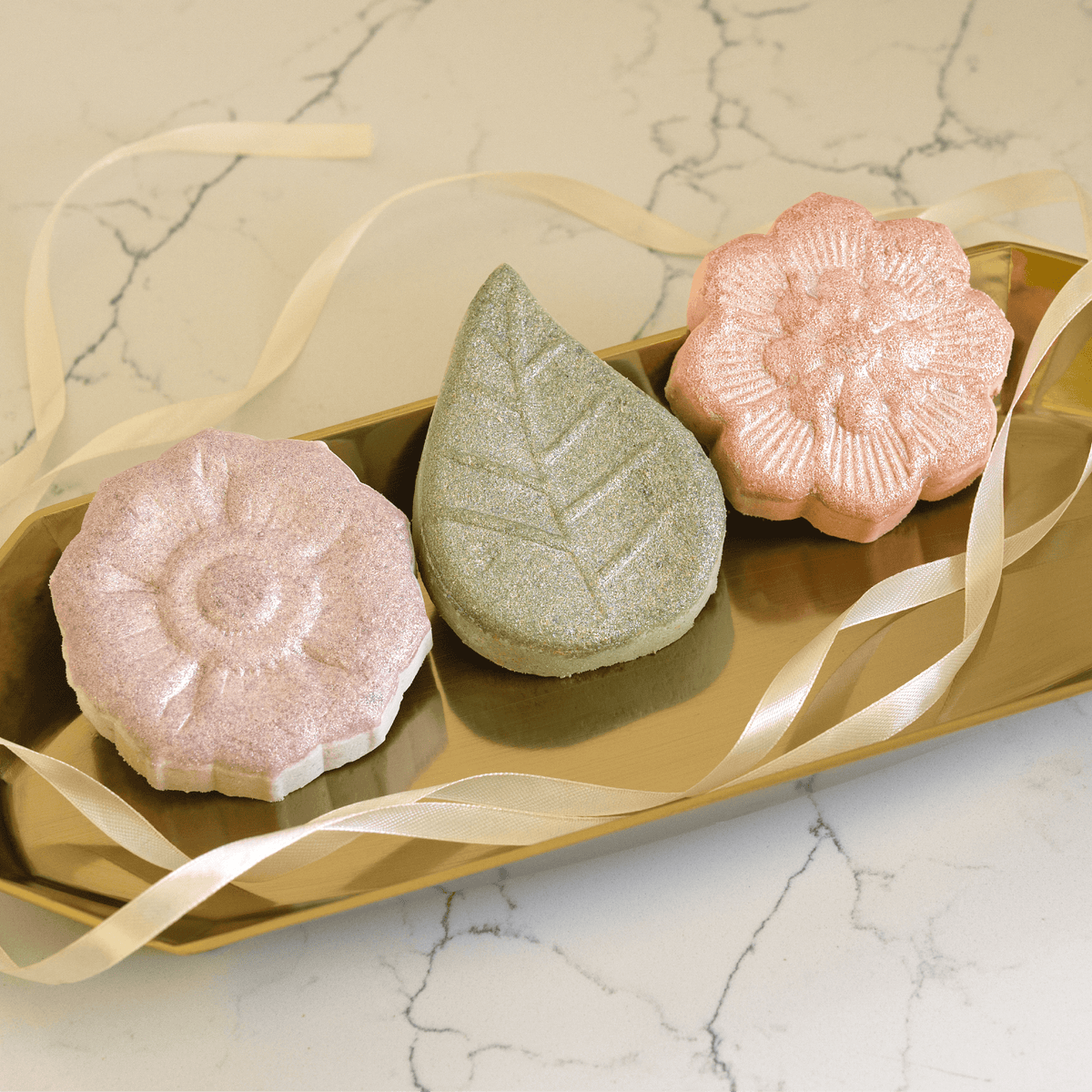 Pacha Soap Co's Signature Bath Bomb Set out of the box, with French Lavender, Vanilla & Sage, and White Blossom & fig lined up on a golden tray with white ribbon draped across it.
