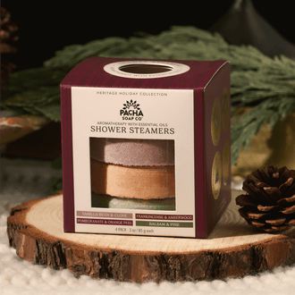 A boxed set of shower steamers from Pacha Soap Co. displayed on a rustic wood slice with evergreen branches and a pinecone.