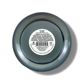 Top-down view of a glass candle with a dark green-gray translucent finish and a white product label in the center