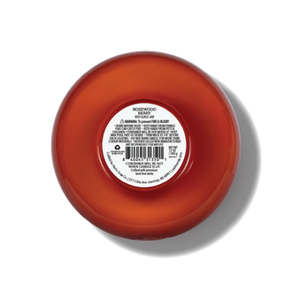 The bottom of a rosewood scented candle, showing a white product information label