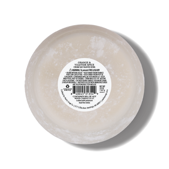 A round, white salt blasted candle bottom with a white label in the center reading 'ORANGE & YULETIDE SPICE'. The candle is photographed from a top-down angle